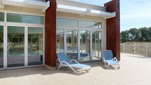 Ein überdachter Außenbereich mit Glastüren, zwei Liegestühlen und einem Pool, der durch die Türen sichtbar ist.