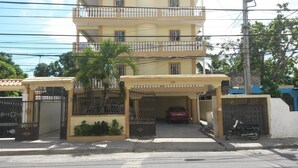 Um edifício residencial com vários andares, portão fechado e um carro estacionado no interior.
