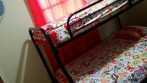 Uma cama de beliche com colchão estampado, cortina vermelha e um ventilador fixado na parede.
