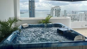 Uma banheira de hidromassagem numa varanda com vista para um edifício alto e um corpo de água.
