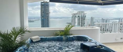 A hot tub on a balcony with a view of a tall building and a body of water.