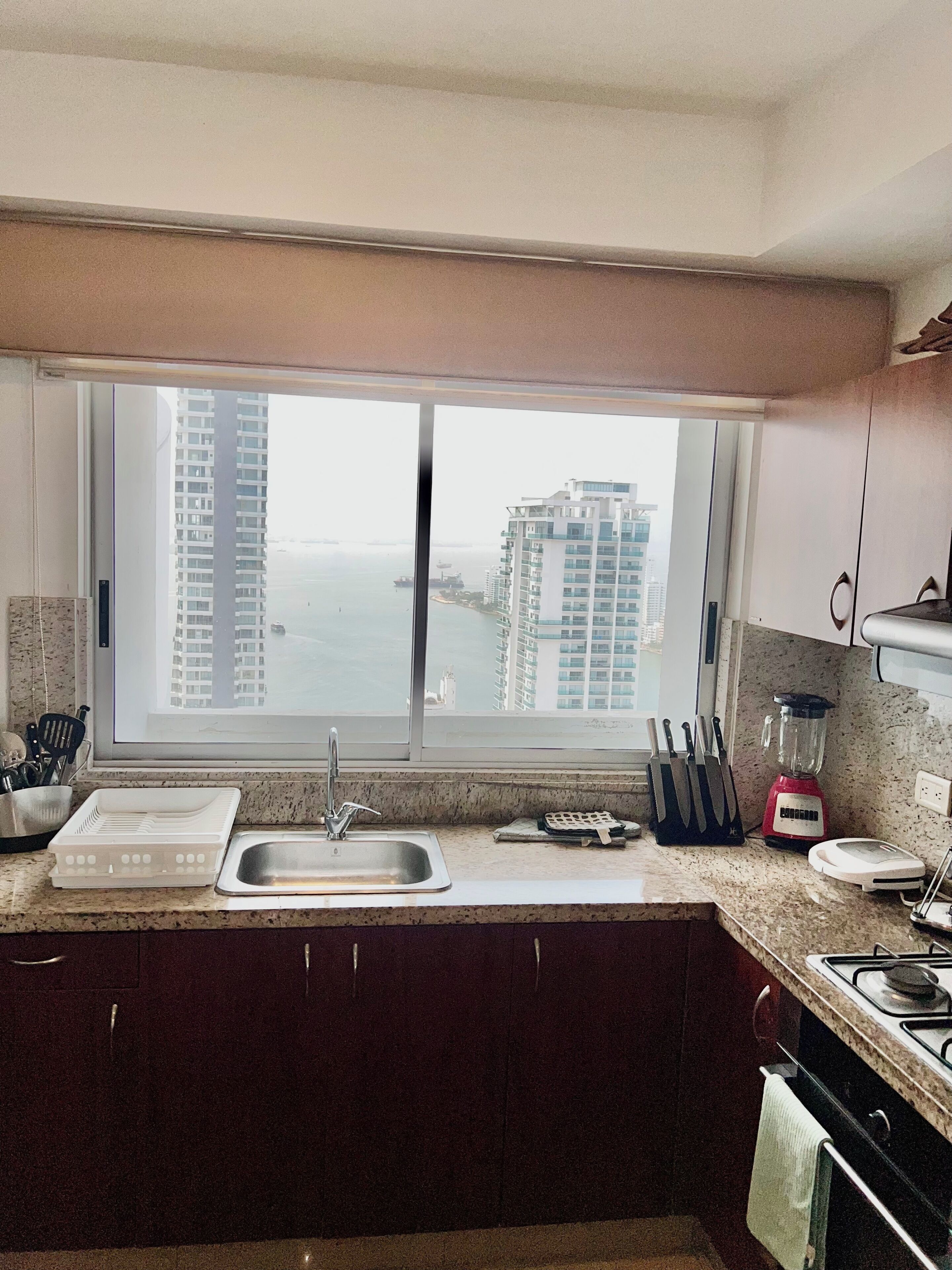 A kitchen with a large window, a sink, a blender, and a stove.