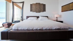 Quarto moderno com uma cama grande, mesa de cabeceira, luminária e uma obra de arte na parede.