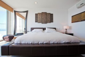 A modern bedroom with a large bed, a side table, a lamp, and a wall-mounted artwork. - Palmetto Penthouse Deluxe Beautiful View and Sunset Floor 39 (Cartagena)