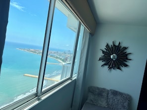 A room with a large window overlooking a coastal cityscape, a decorative metal wall piece, and a cushioned bench. - Palmetto Suite Superior 3901 (Cartagena)