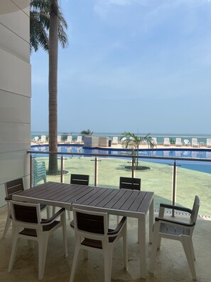 Un balcón con mesa y sillas, con vista a una piscina y al océano.