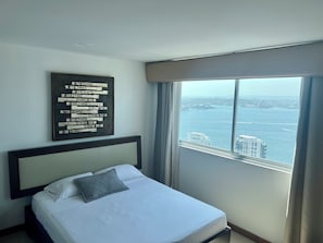 A hotel room with a bed, a large window with a city view, and a framed artwork on the wall. - Palmetto Suite Superior 3901 (Cartagena)