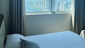 Ein Hotelzimmer mit einem großen Bett, Blick auf eine Stadtlandschaft durch ein Fenster und Vorhängen.
