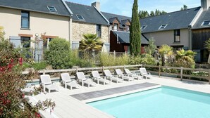 Ein Swimmingpool mit Liegestühlen, umgeben von Häusern mit steinernen Fassaden und Satteldächern.