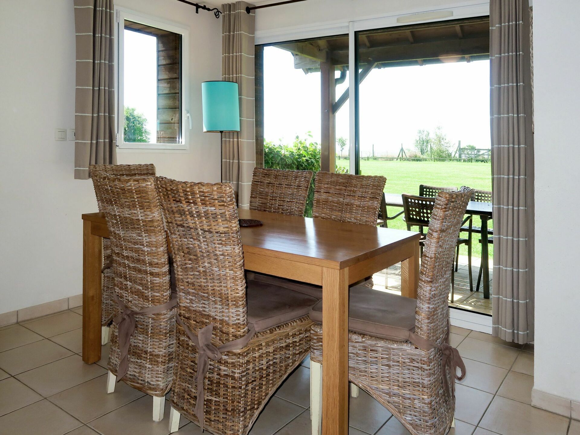 A dining area with a wooden table and wicker chairs, a lamp, and a view of the outdoors.