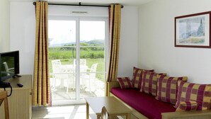 Habitación con sofá, mesa, televisión y vista a un paisaje verde a través de un ventanal.