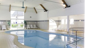 Una piscina interior con suelo de baldosas, una escalera de piscina y sillones de descanso alrededor del borde.