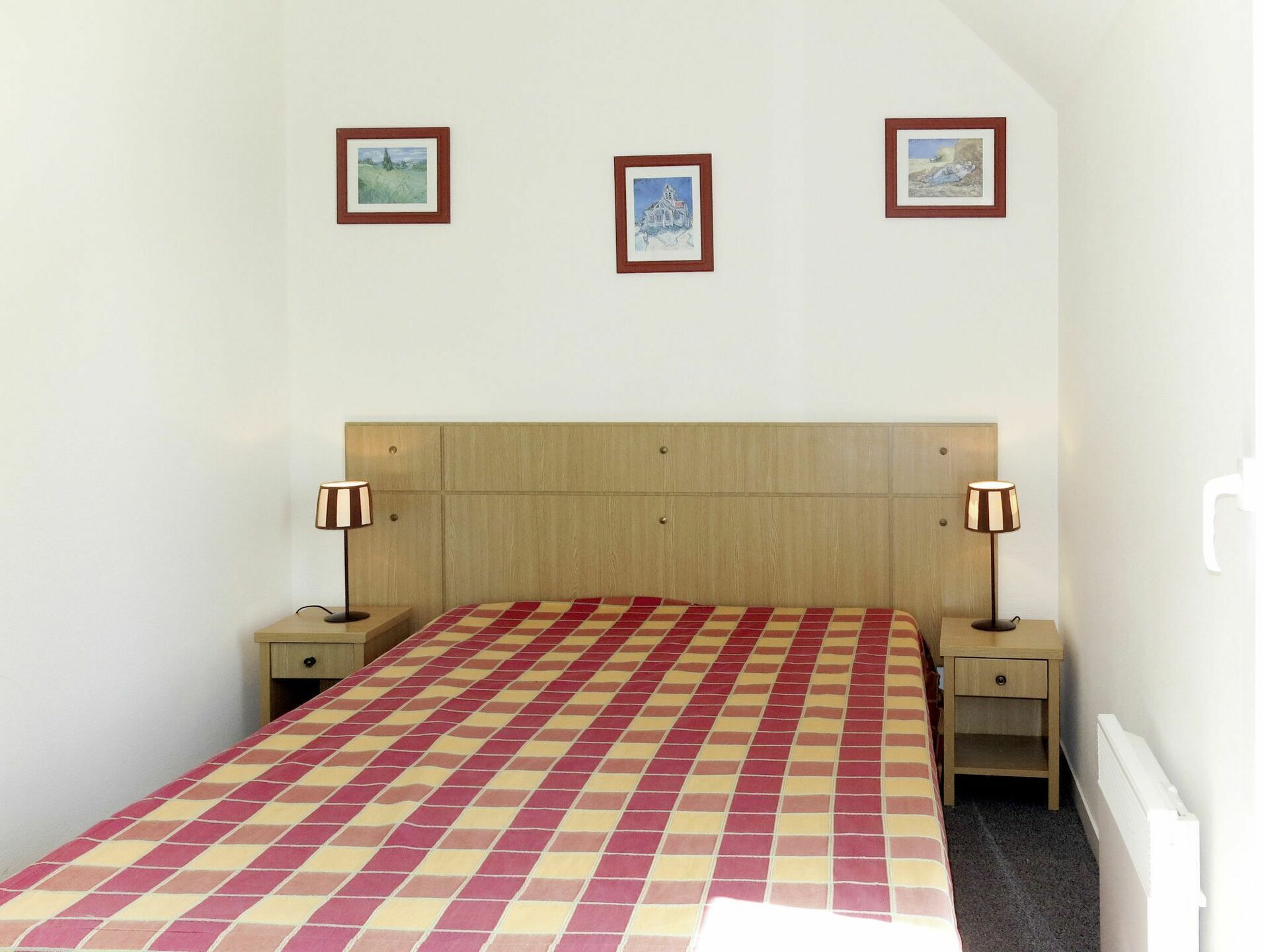 A bedroom with a checkered bedspread, two bedside lamps, and three framed pictures on the wall.