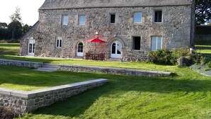 A stone building with a sloped roof, a red umbrella, and a stone bench outside. - Charming Breton house with all comforts (ST ADRIEN)