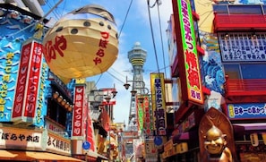 A busy urban street with various shops and signs, a prominent tower in the background, and a large spherical object.