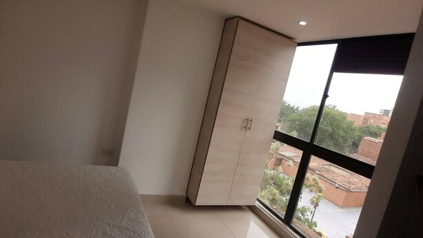 Quarto com guarda-roupa espaçoso, cama e janela com vista para edifícios e árvores.