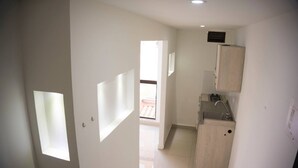 Um corredor estreito com uma pequena cozinha, uma janela e uma porta para outro espaço.