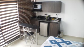 Eine kompakte Küche mit Mikrowelle, Spüle und kleinem Kühlschrank. Ein Barhocker und ein gemustertes Teppich sind vorhanden.