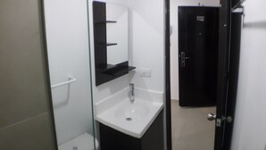 Ein kleines, modernes Badezimmer mit einem weißen Waschbecken, einem schwarzen Schrank und einem Spiegel über dem Waschbecken.