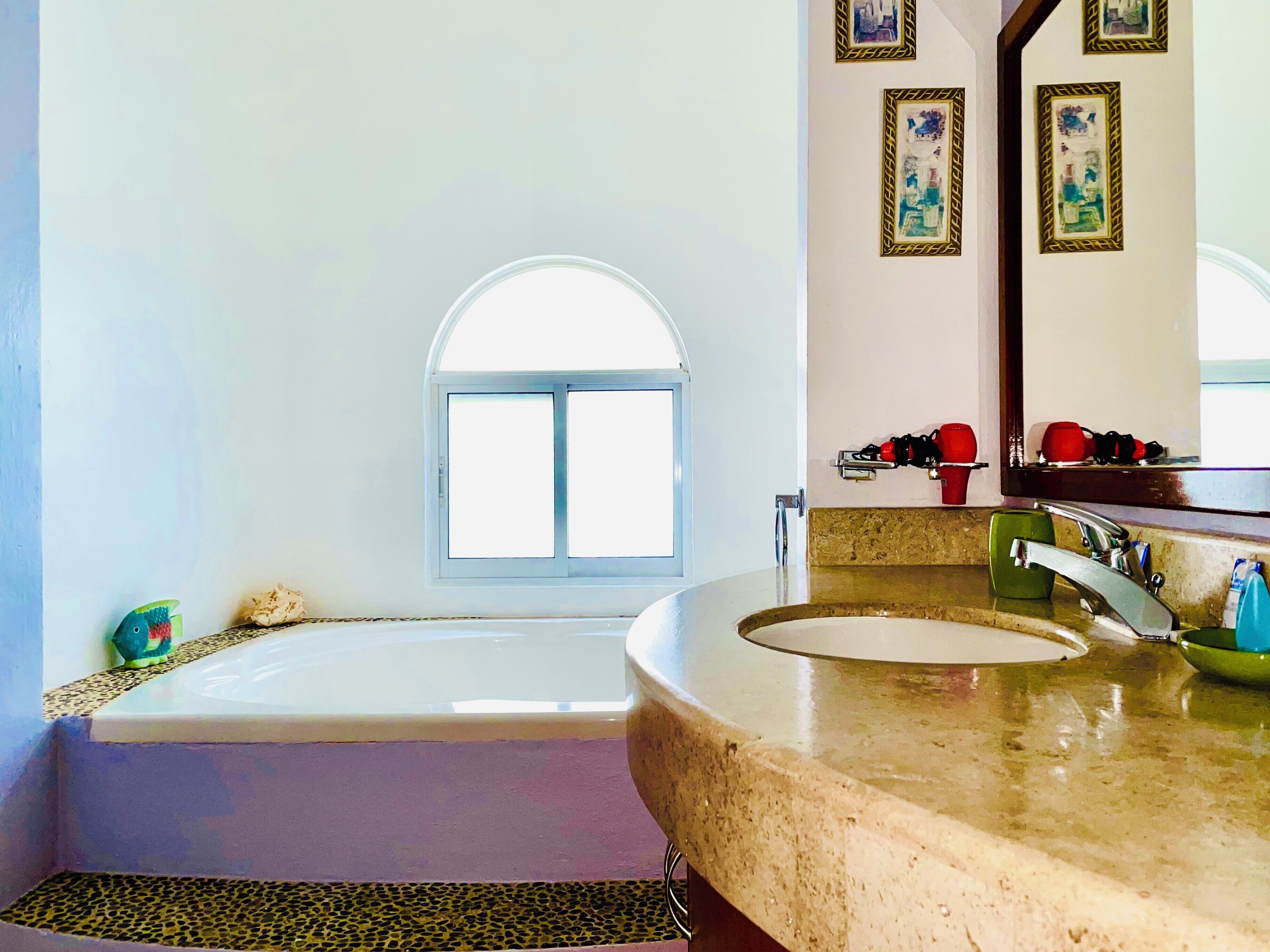 Un baño con bañera, lavamanos, ventana y espejo.
