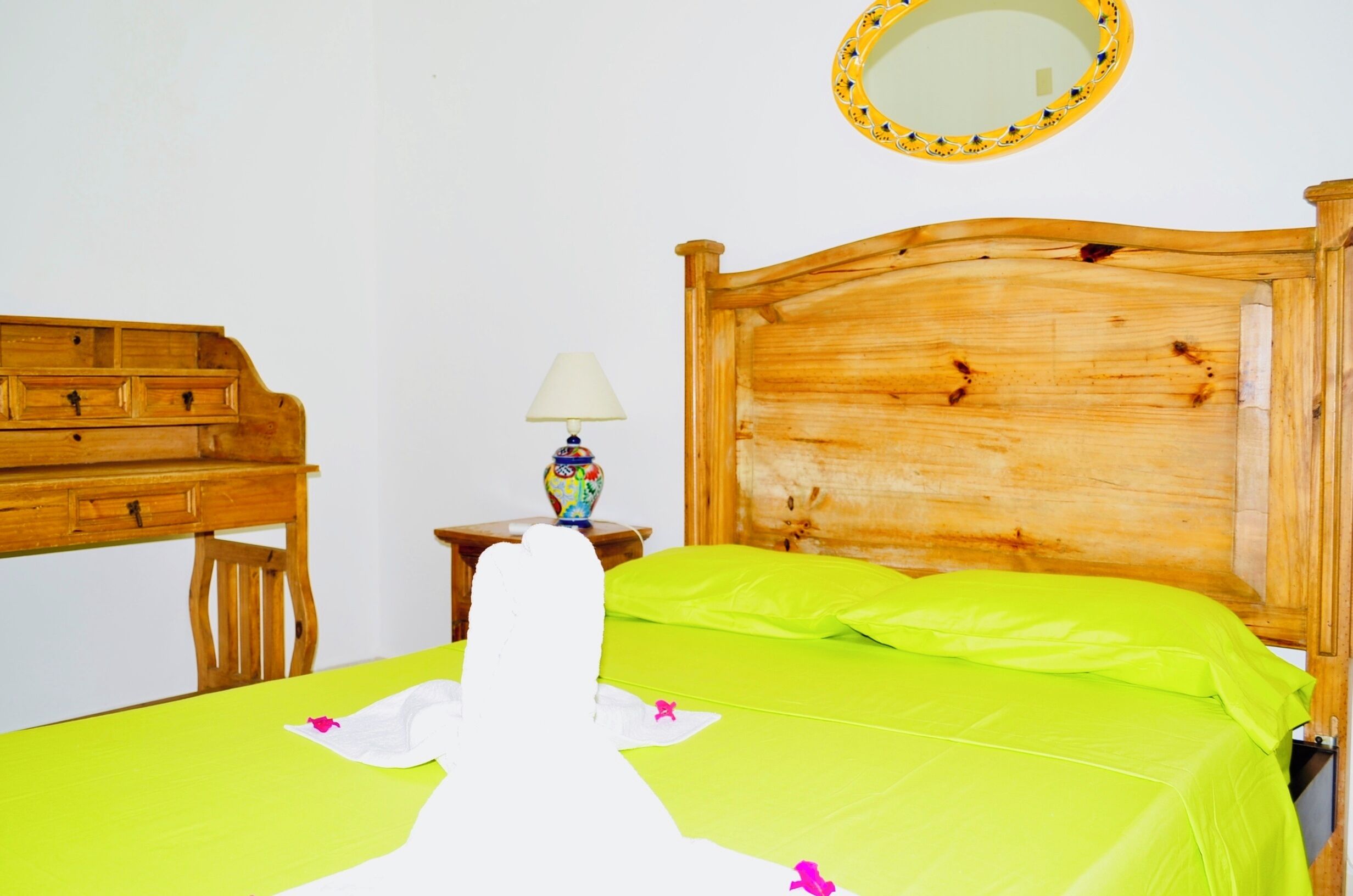 A wooden bed with a green bedspread and pillows, a wooden nightstand with a lamp, and a wooden dresser with drawers.