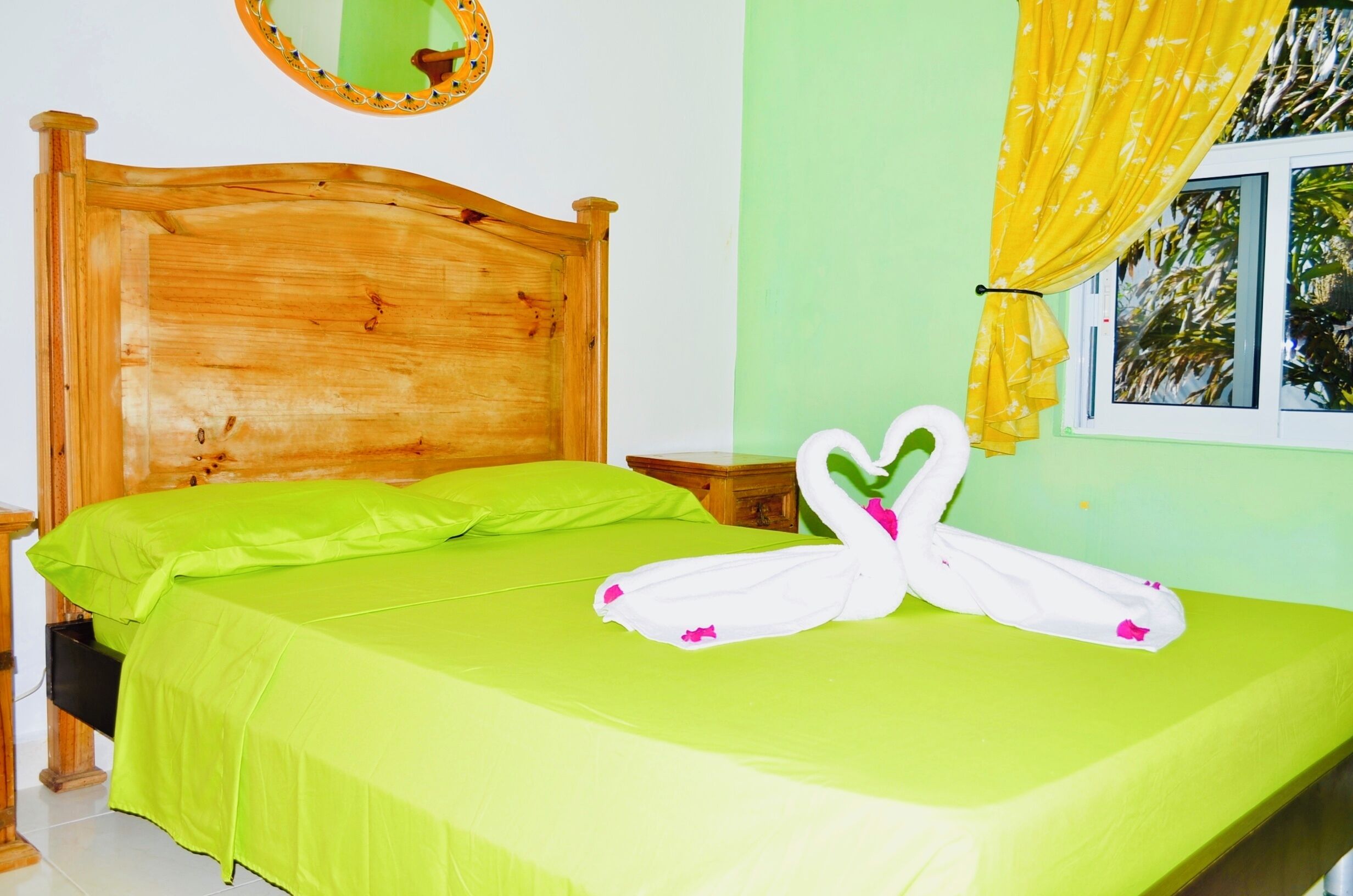 A bed with a green bedspread and two white towels shaped like swans.