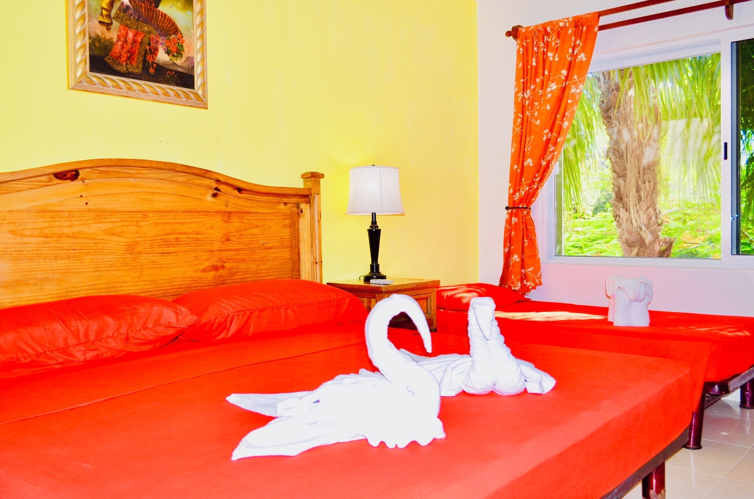 A bed with a wooden headboard, a nightstand with a lamp, a window with curtains, and a framed picture on the wall.