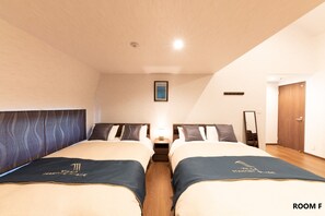 Quarto de hotel com duas camas, uma mesa de cabeceira, um quadro na parede e uma porta de madeira.
