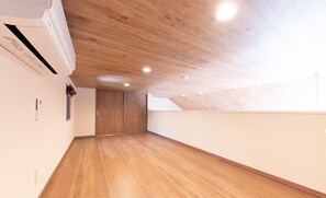 A spacious attic room with wooden flooring, a sloped ceiling, and a visible air conditioning unit.