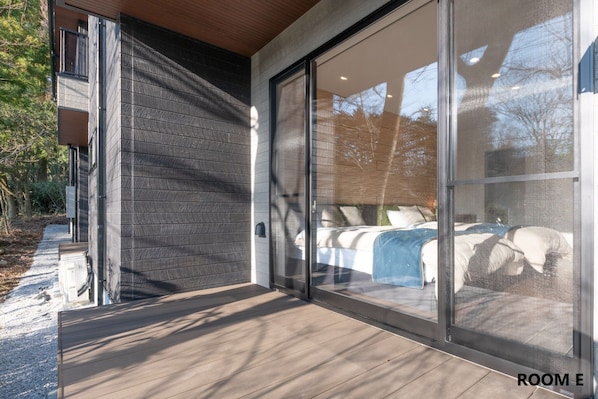 A modern building with a large sliding glass door leading to a bedroom with a bed and pillows.