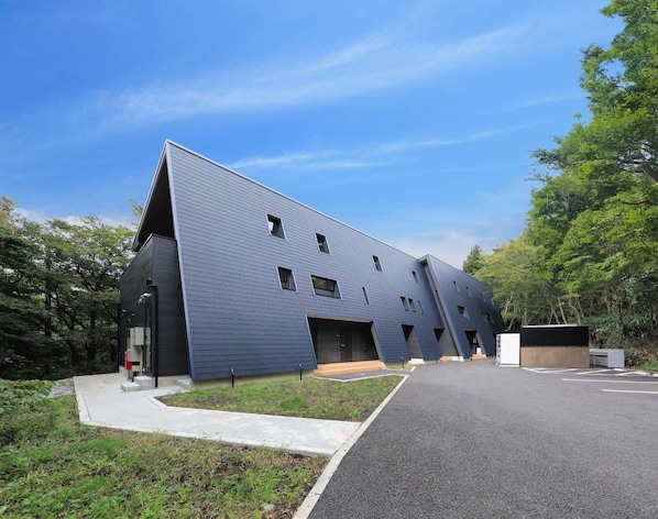 A modern building with a sloped roof, multiple windows, and a paved entrance area.