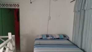 Una cama individual con una colcha a rayas en una habitación con paredes blancas, una puerta verde y una barandilla blanca.