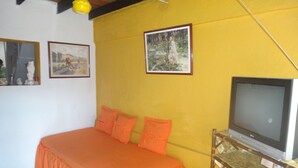 A bedroom with a bed, orange bedding, a TV on a stand, and two framed pictures on the wall. - Room-green Sea Inn San Luis (San Andrés)