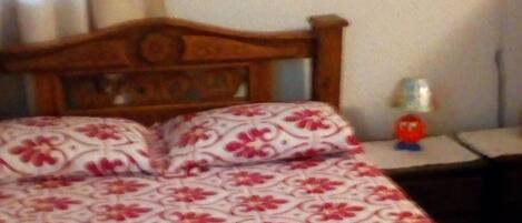 A bedroom with a wooden bed, a wall-mounted cross, and a bedside table with a lamp.