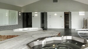 Un área de spa con un amplio jacuzzi, una terraza de madera y una decoración interior moderna.