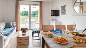Una sala de estar moderna con un sofá, una mesa de comedor con mariscos y un televisor montado en la pared.