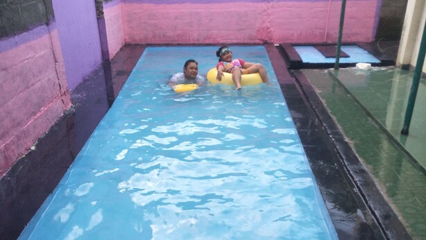 A narrow indoor pool with two people on inflatable rings. - D Kir's Homestay (Depok)