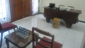 A room with a wooden door, a table with water bottles, a chair, a desk with a computer, and a decorative vase. - D Kir's Homestay (Depok)