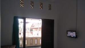 A room with a bed, a TV mounted on the wall, and a sliding glass door leading to an outdoor area. - D Kir's Homestay (Depok)