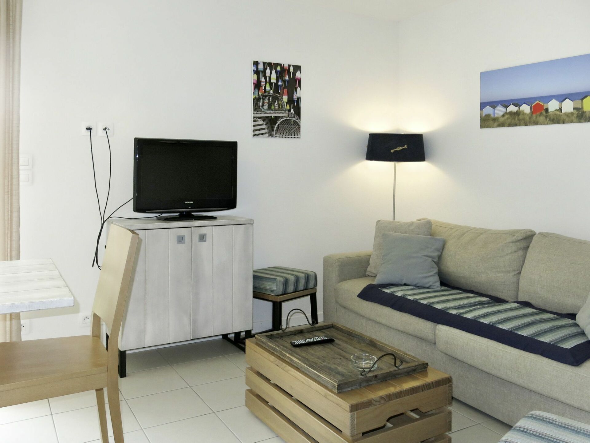 Un salon avec un téléviseur posé sur un meuble, un canapé avec des coussins, une table basse et une lampe.
