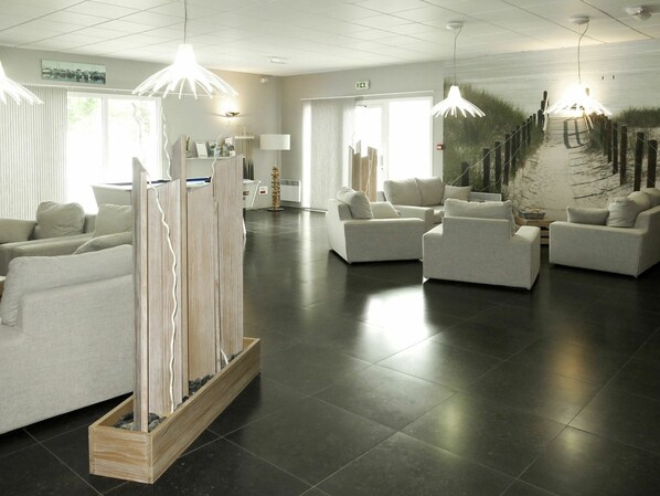 A modern hotel lobby with a seating area, a reception desk, and a large window.