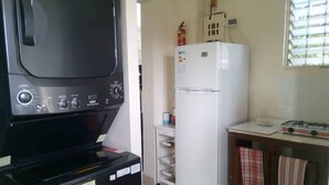A compact kitchen with a stove, refrigerator, and a black appliance with control knobs. - Hostal Arboleda, Colonial Zone, Santo Domingo (Santo Domingo)