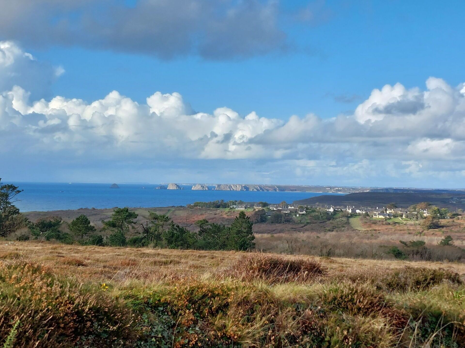 A coastal landscape with a village, rolling hills, and a clear sky.