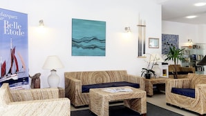 Ein Zimmer mit Korbmöbeln, einem blauen abstrakten Gemälde, einem Plakat und einem Bücherregal.