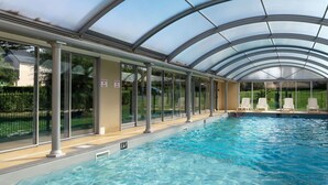 Ein Hallenbad mit klarem Wasser, umgeben von Glaswänden und Säulen, mit einer überdachten Dachkonstruktion.
