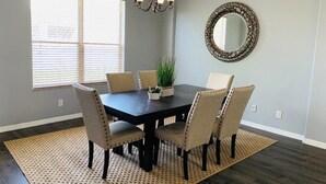 A dining room with a dark wooden table, six beige upholstered chairs, a chandelier, a large mirror, and a window with blinds. - Near Img And Siesta Key Beach Paradise Home (Bradenton)