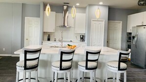 A modern kitchen with a central island, white cabinetry, and four bar stools. - Near Img And Siesta Key Beach Paradise Home (Bradenton)