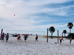 A beach volleyball game with a net and palm trees in the background.