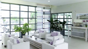 Un salón moderno con sofás blancos, una mesa de centro y grandes ventanas con vistas al exterior.