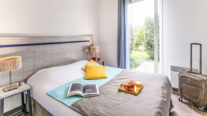 Ein Hotelzimmer mit einem Bett, einem Nachttisch mit Lampe, einem Koffer und einem Frühstückswagen mit Croissants und Saft.